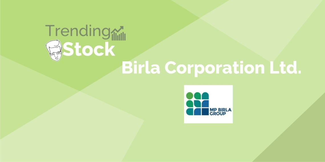 A man in a business suit standing in front of a green backdrop with the birla corporation logo and the text 
